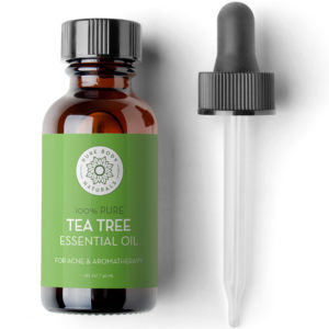 A bottle of Tea Tree Essential Oil, 1 fl oz is placed next to a dropper. The bottle has a green label with text indicating it's for acne and aromatherapy. The bottle holds 1 fluid ounce (30 ml) of the essential oil.