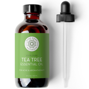 A dark amber glass bottle labeled "Tea Tree Essential Oil, 4 fl oz," with a green label featuring a floral logo. A black dropper is placed beside the bottle.